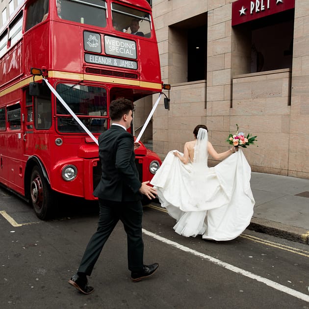 a bride and groom walking towards their red London bus