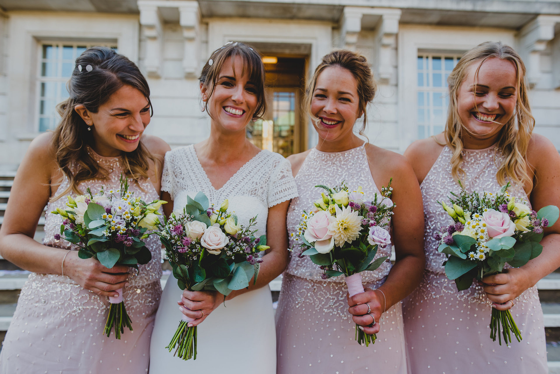 a bride with three bridesmaids dressed in pink holding bouquets