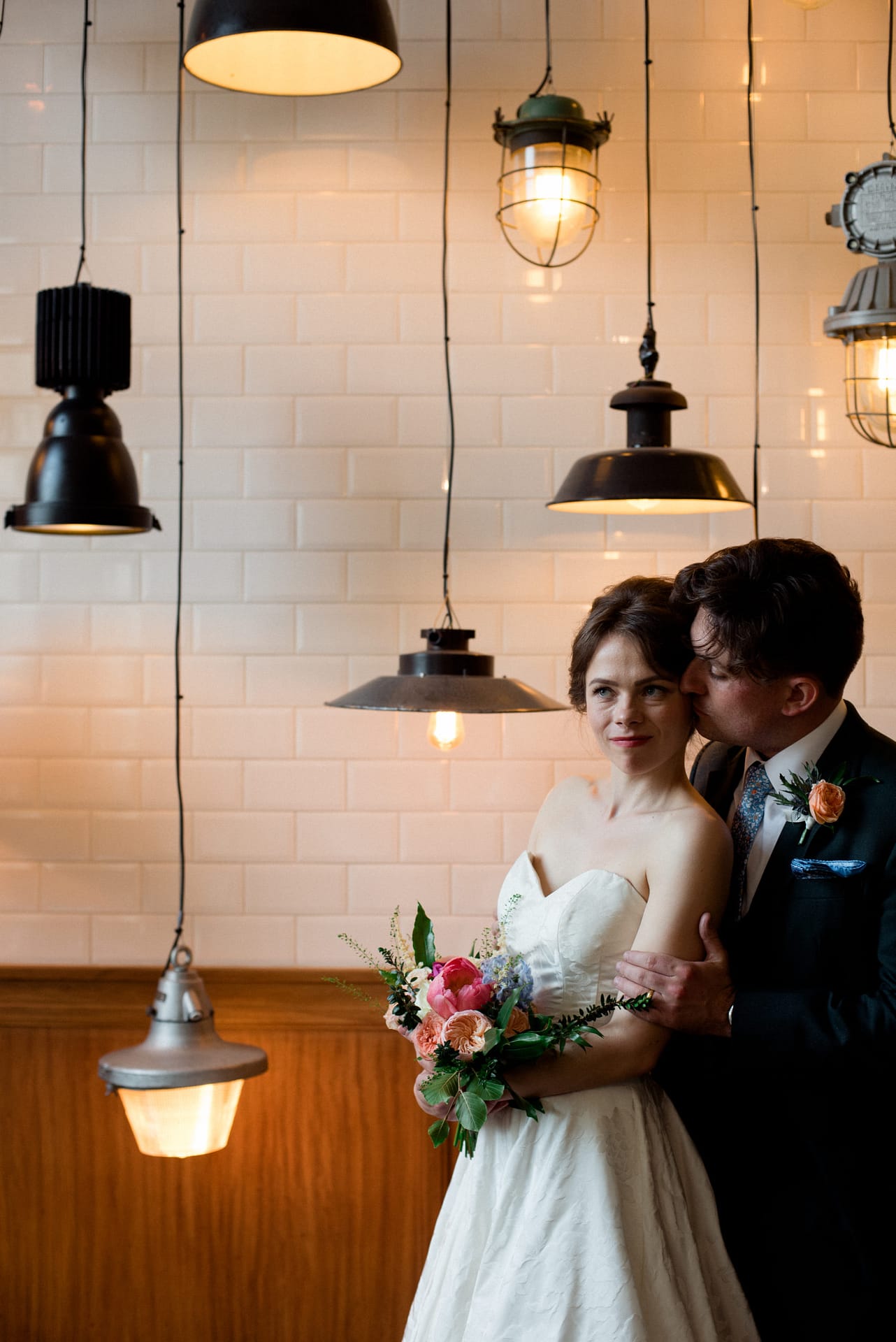 a portrait of a groom hugging his bride surrounded by interesting lamp shades